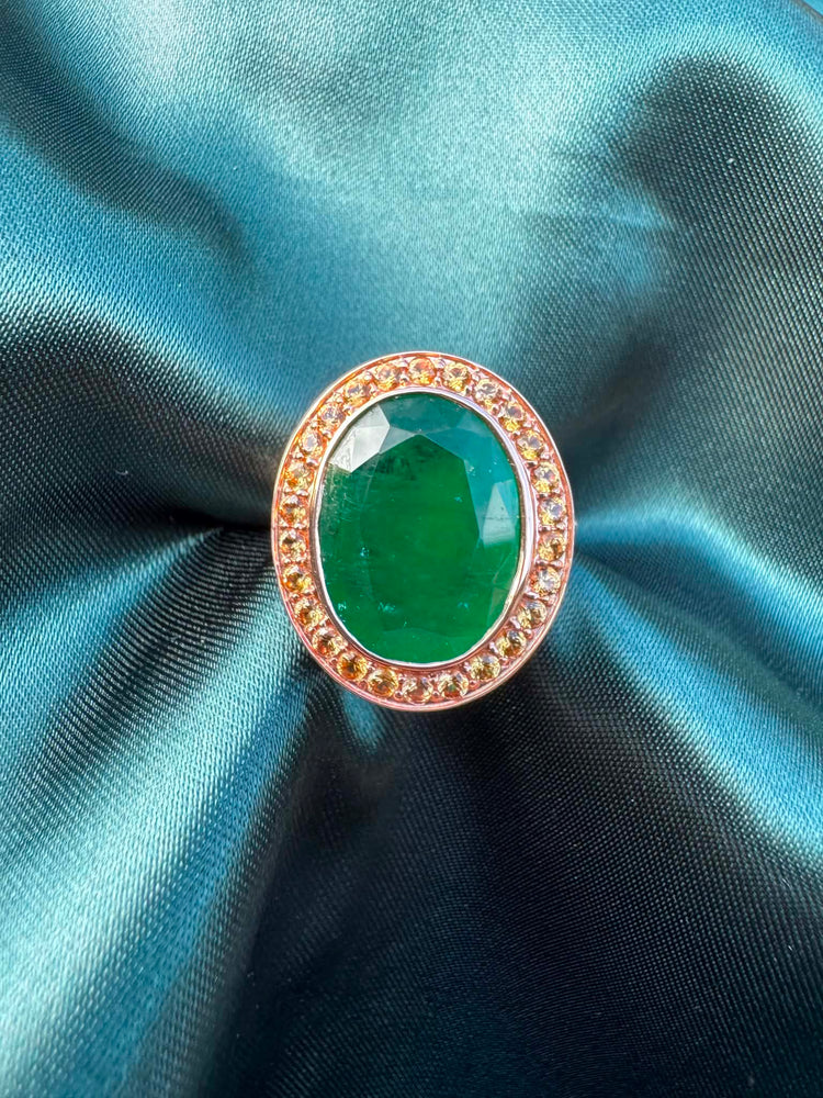 Emerald and orange sapphire cocktail ring in 14ct rose gold, front view showing oval emerald in sapphire halo