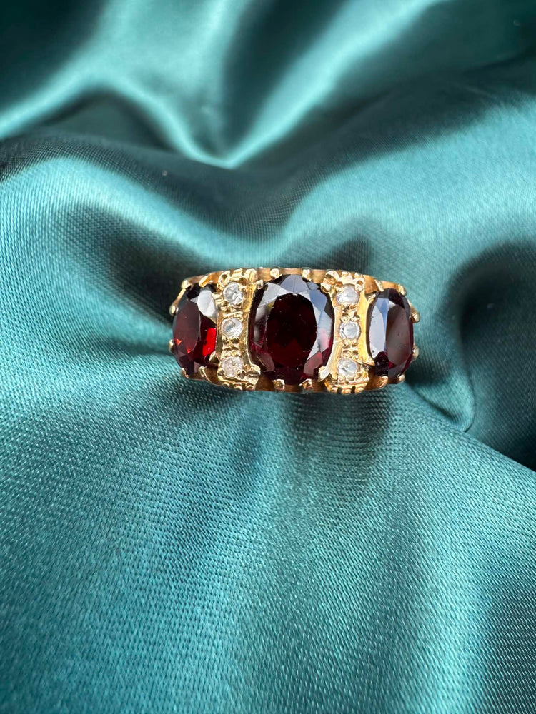 Garnet and paste three stone ring in 9ct gold on teal fabric, front view showing garnet and paste stones