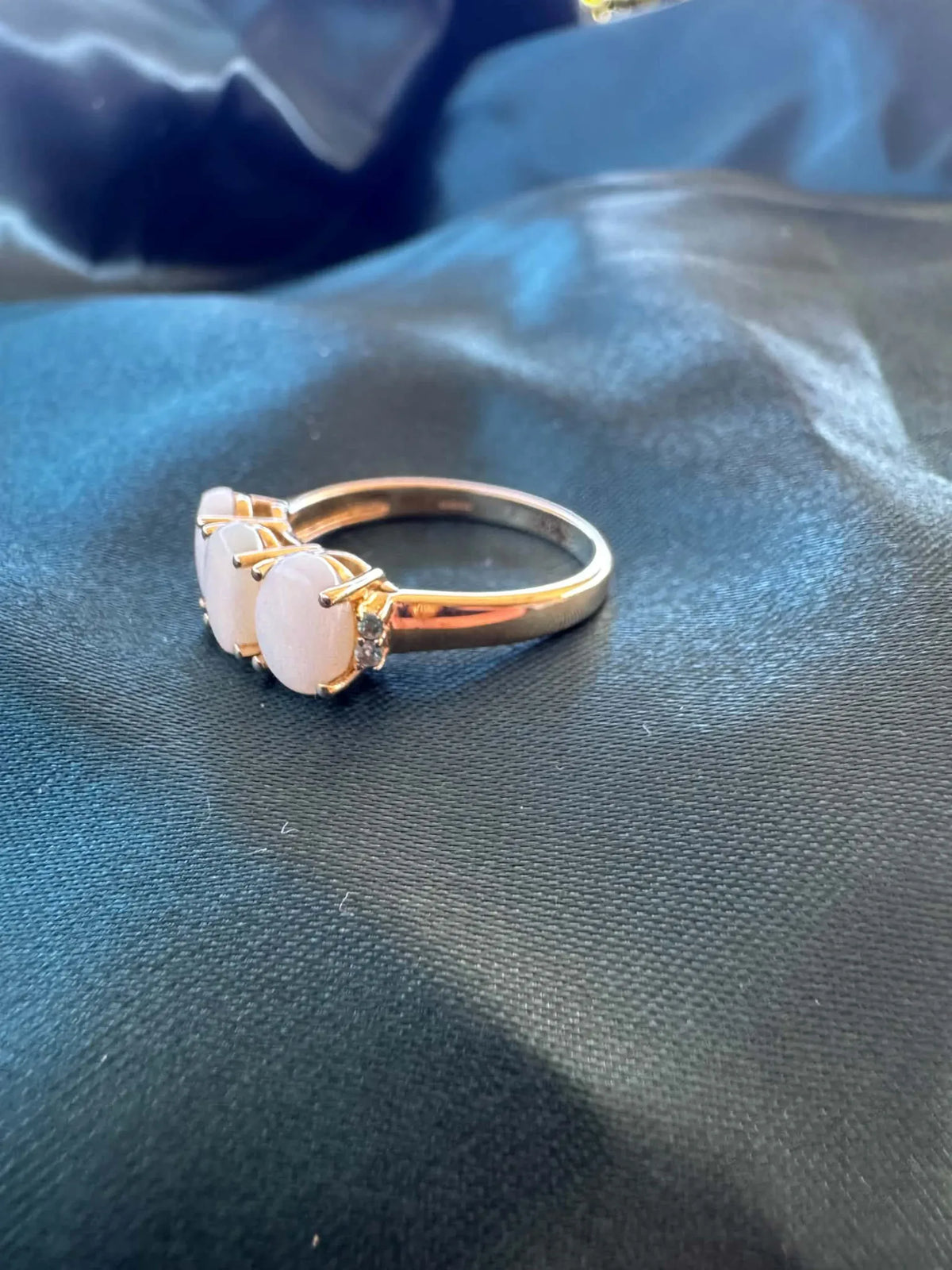Three-stone white opal ring in 9ct yellow gold, angled side view showing three oval white opal cabochons and gold band