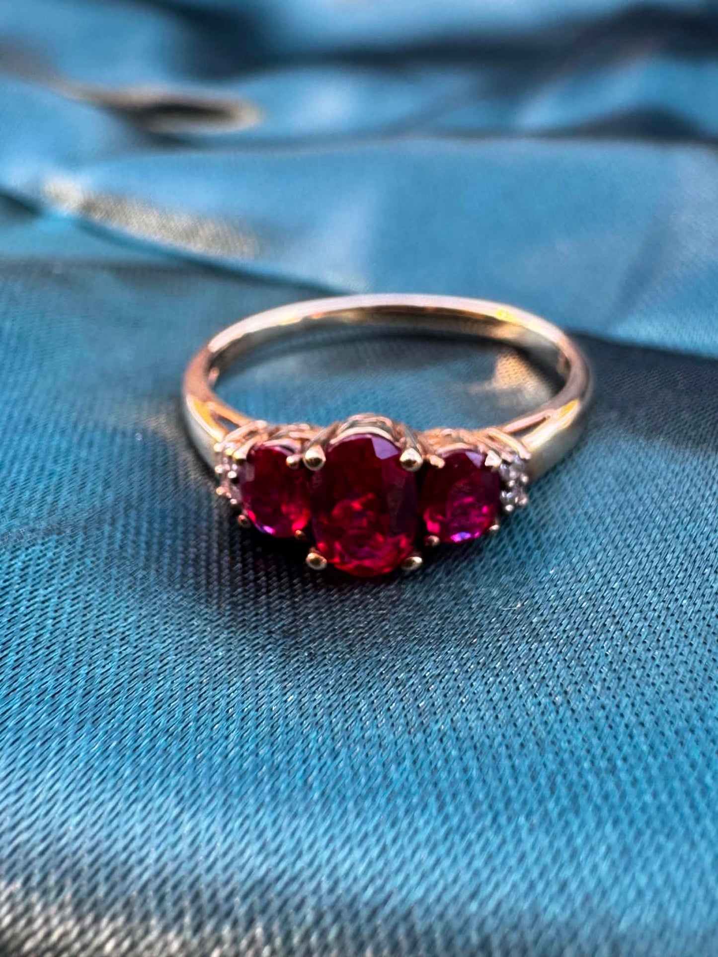 Ruby and diamond trilogy ring in 9ct yellow gold, front view showing three oval rubies