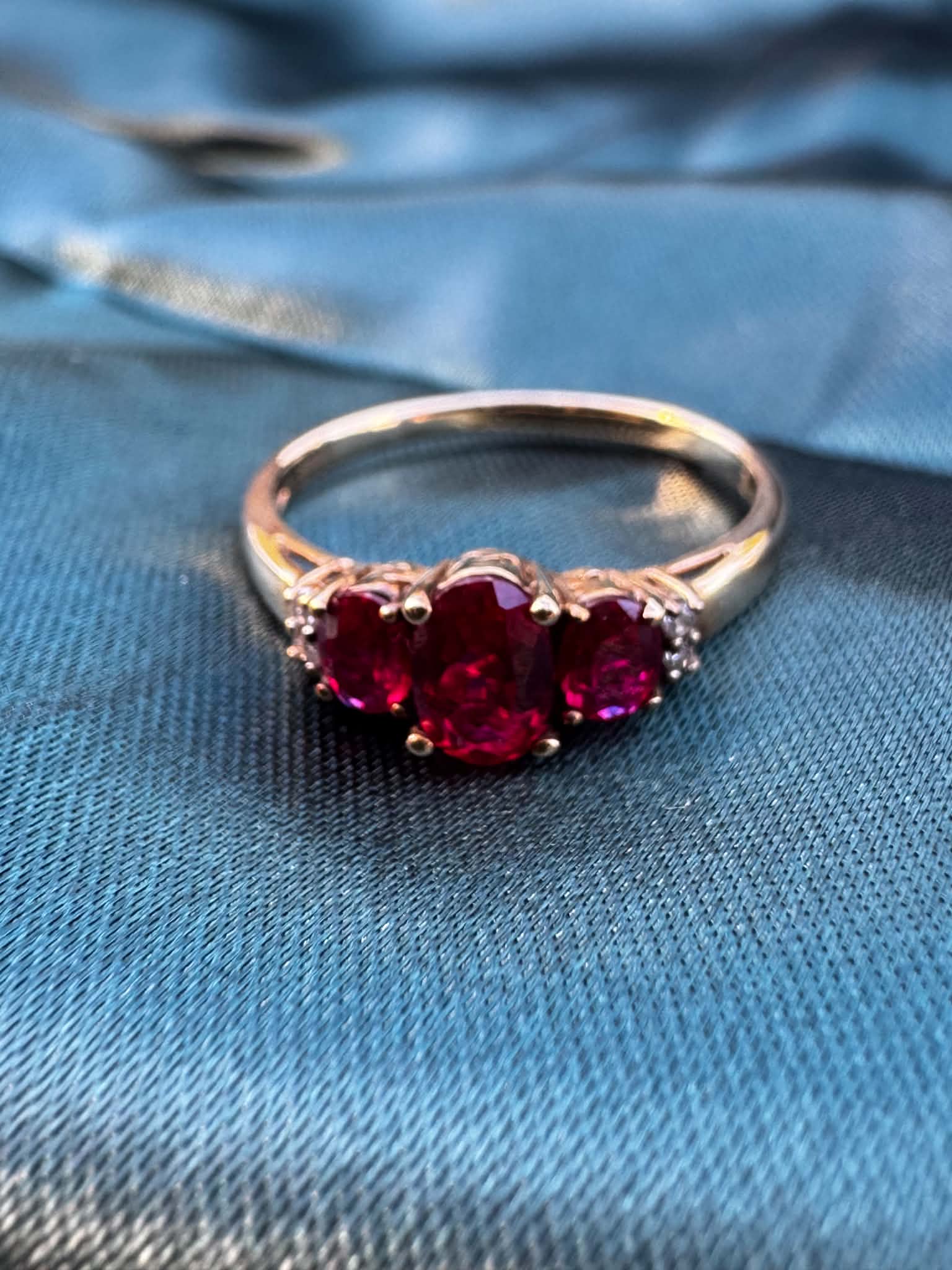 Ruby and diamond trilogy ring in 9ct yellow gold, front view showing three oval rubies