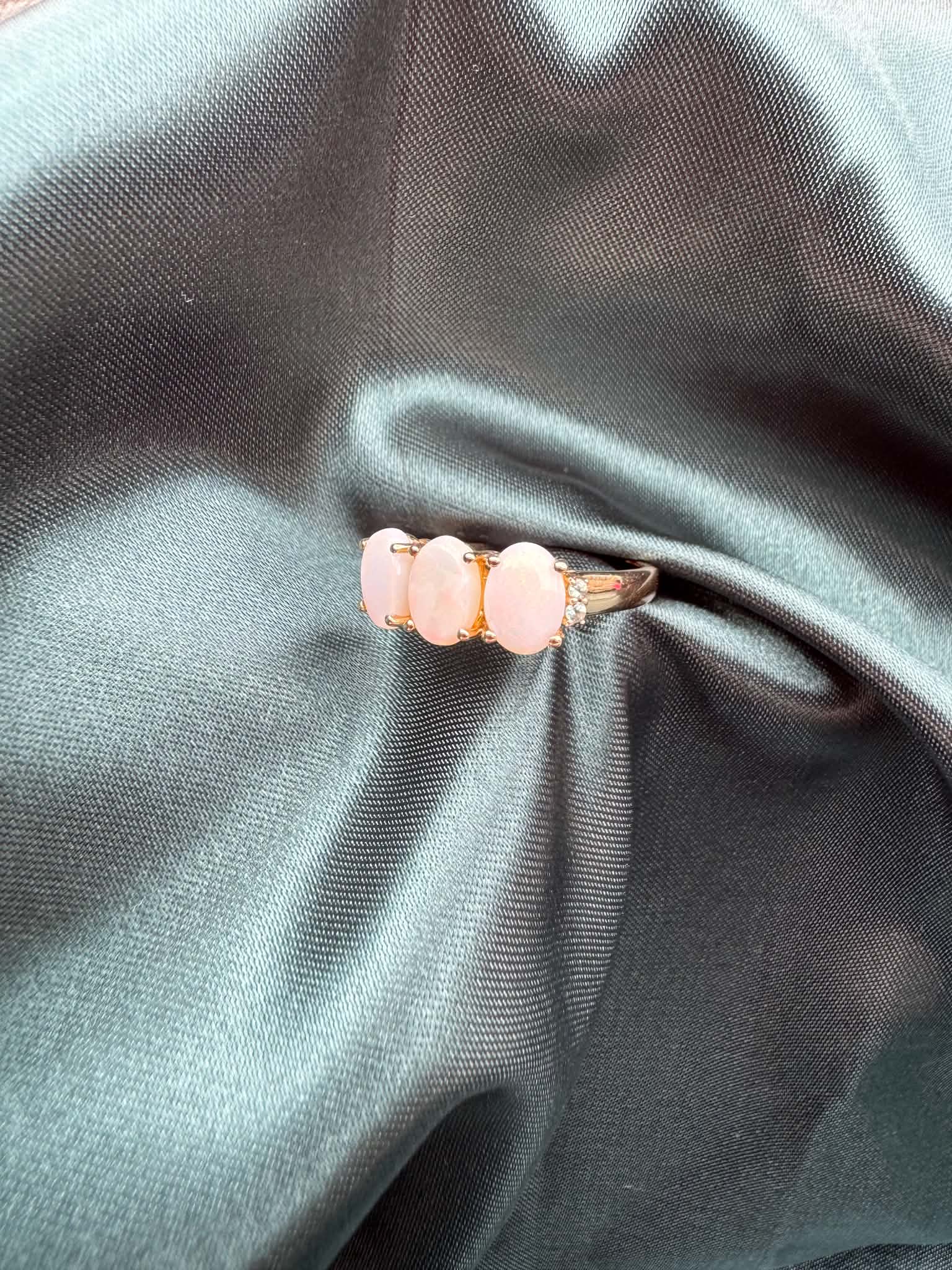 Three-stone white opal ring in 9ct yellow gold, angled front view showing white opal and green accent gemstones