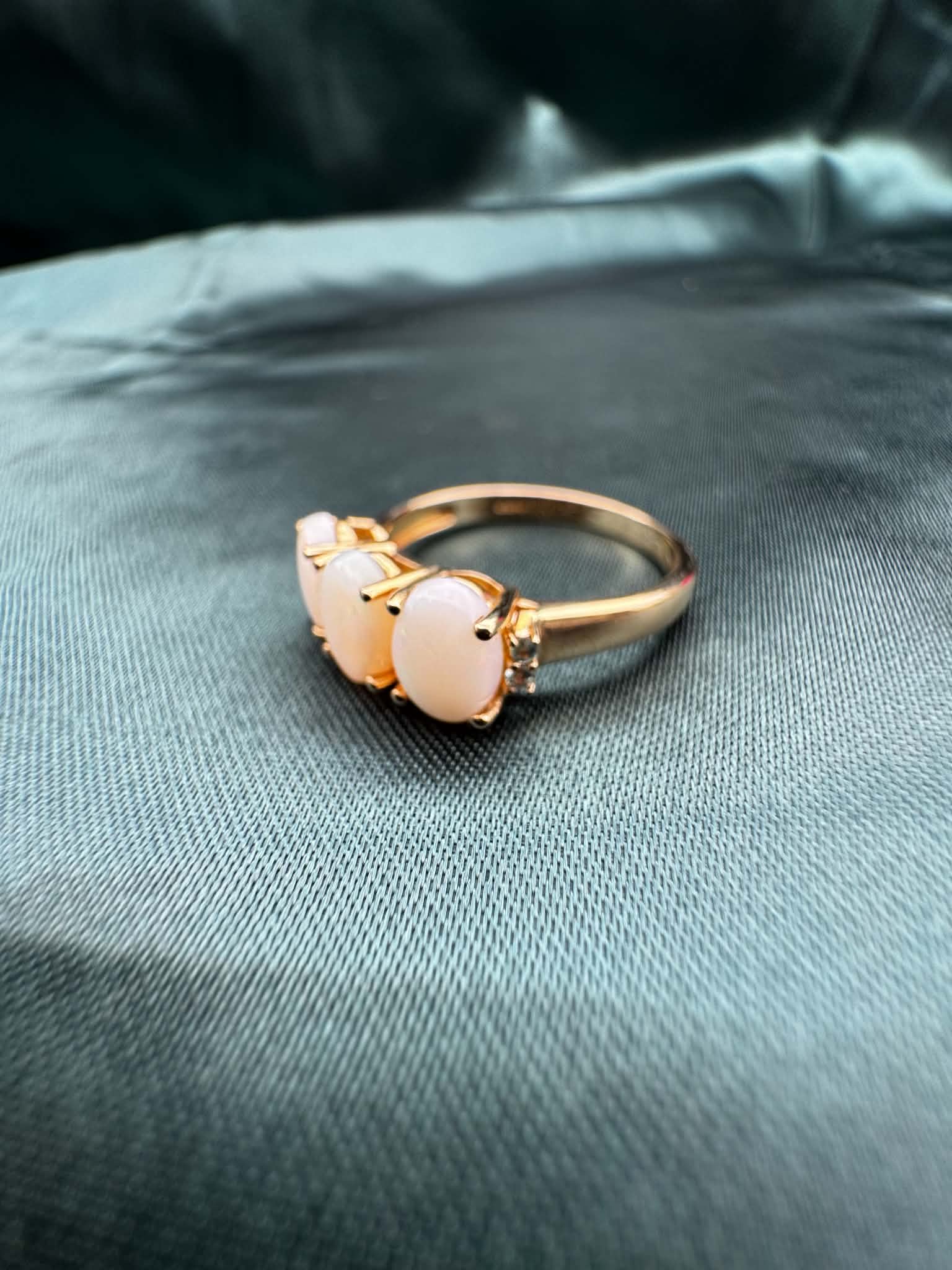 Three-stone white opal ring in 9ct yellow gold, angled top view showing white opal, green accent gemstones and gold band