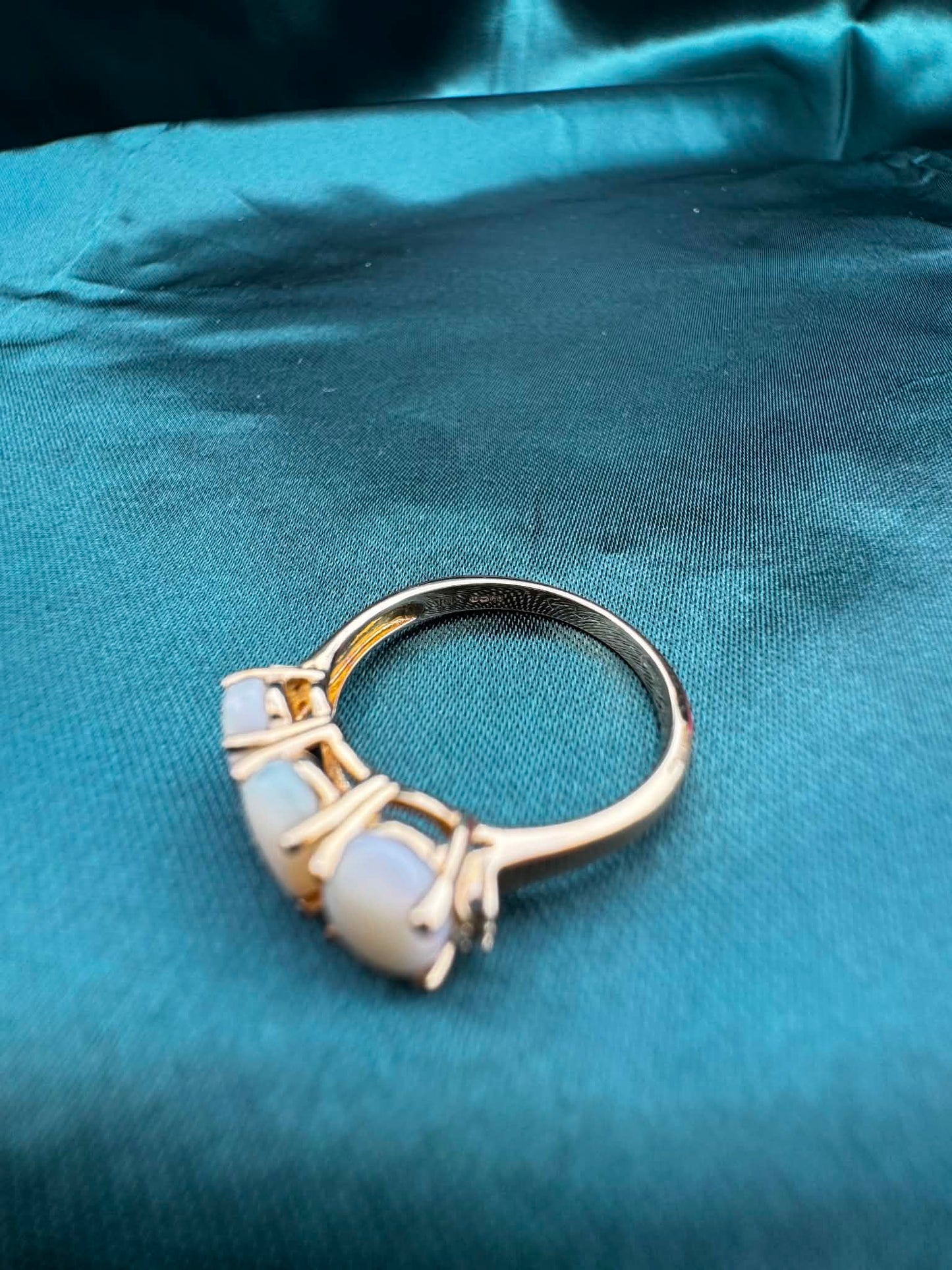 Three-stone white opal ring in 9ct yellow gold, angled top view showing white opal, green accent gemstones and gold band