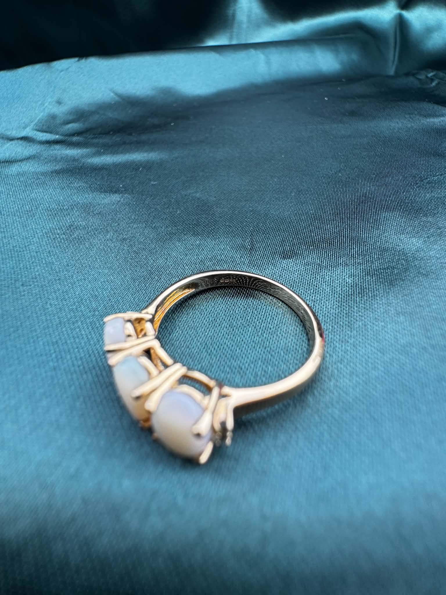 Three-stone white opal ring in 9ct yellow gold, angled top view showing white opal, green accent gemstones and gold band