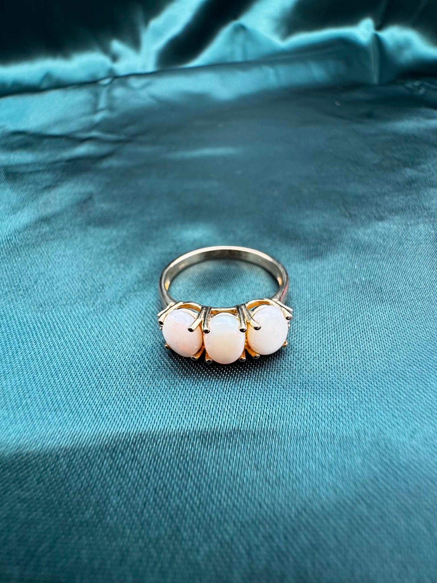 Three-stone white opal ring in 9ct yellow gold, top view showing white opal and green accent gemstones