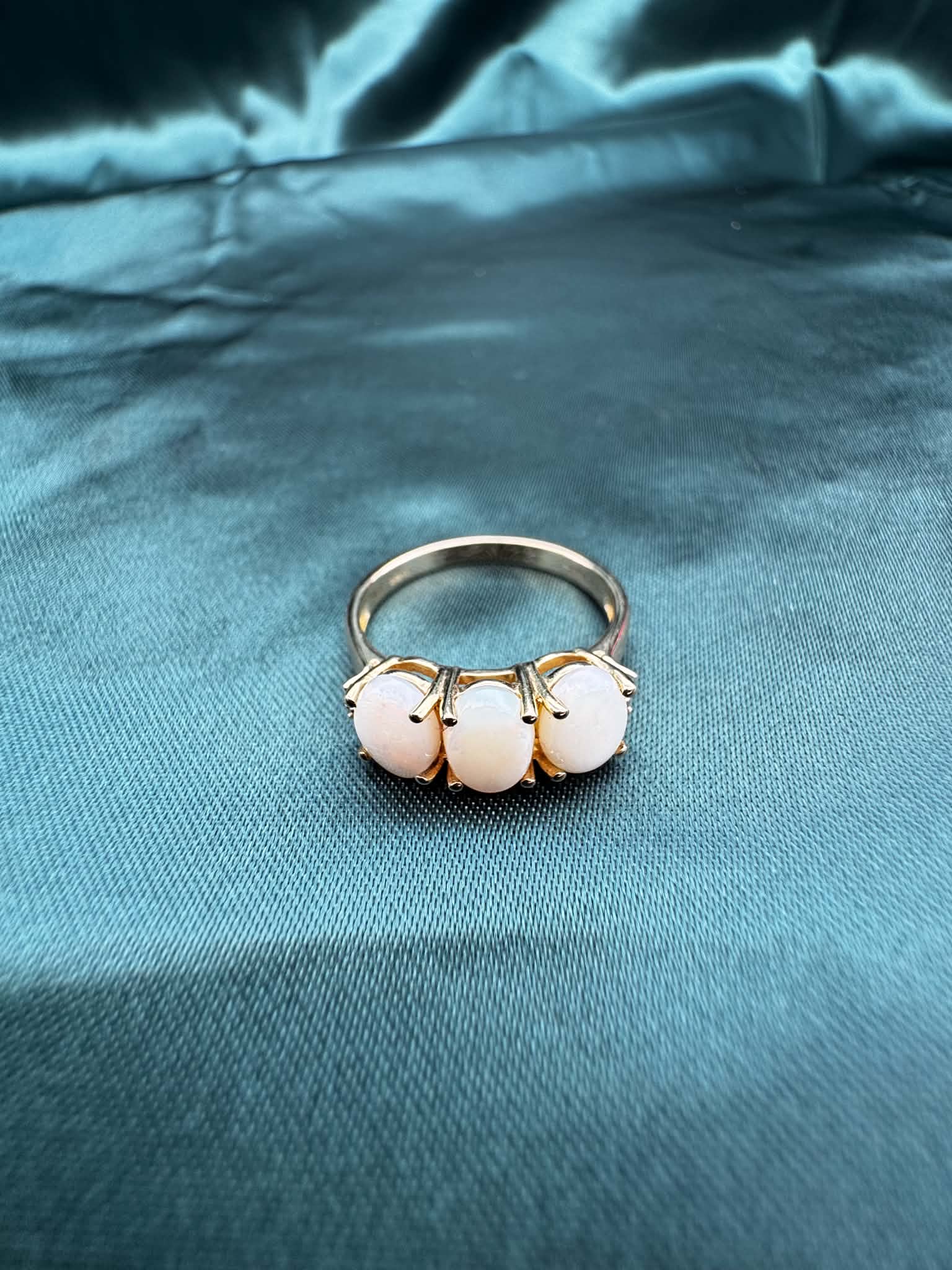 Three-stone white opal ring in 9ct yellow gold, top view showing white opal and green accent gemstones