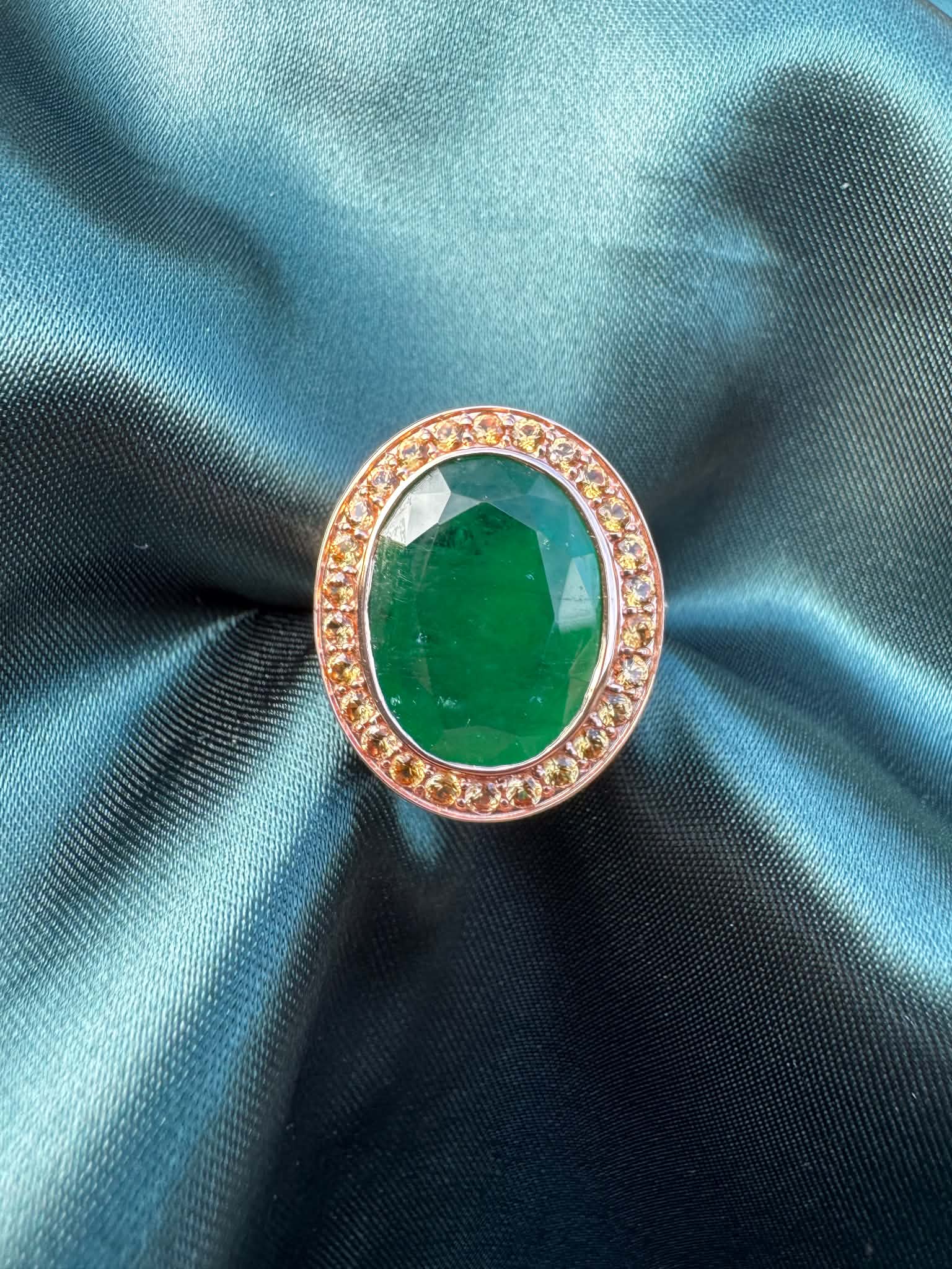 Emerald and orange sapphire cocktail ring in 14ct rose gold, front view showing oval emerald in sapphire halo