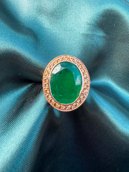 Emerald and orange sapphire cocktail ring in 14ct rose gold, front view showing oval emerald in sapphire halo