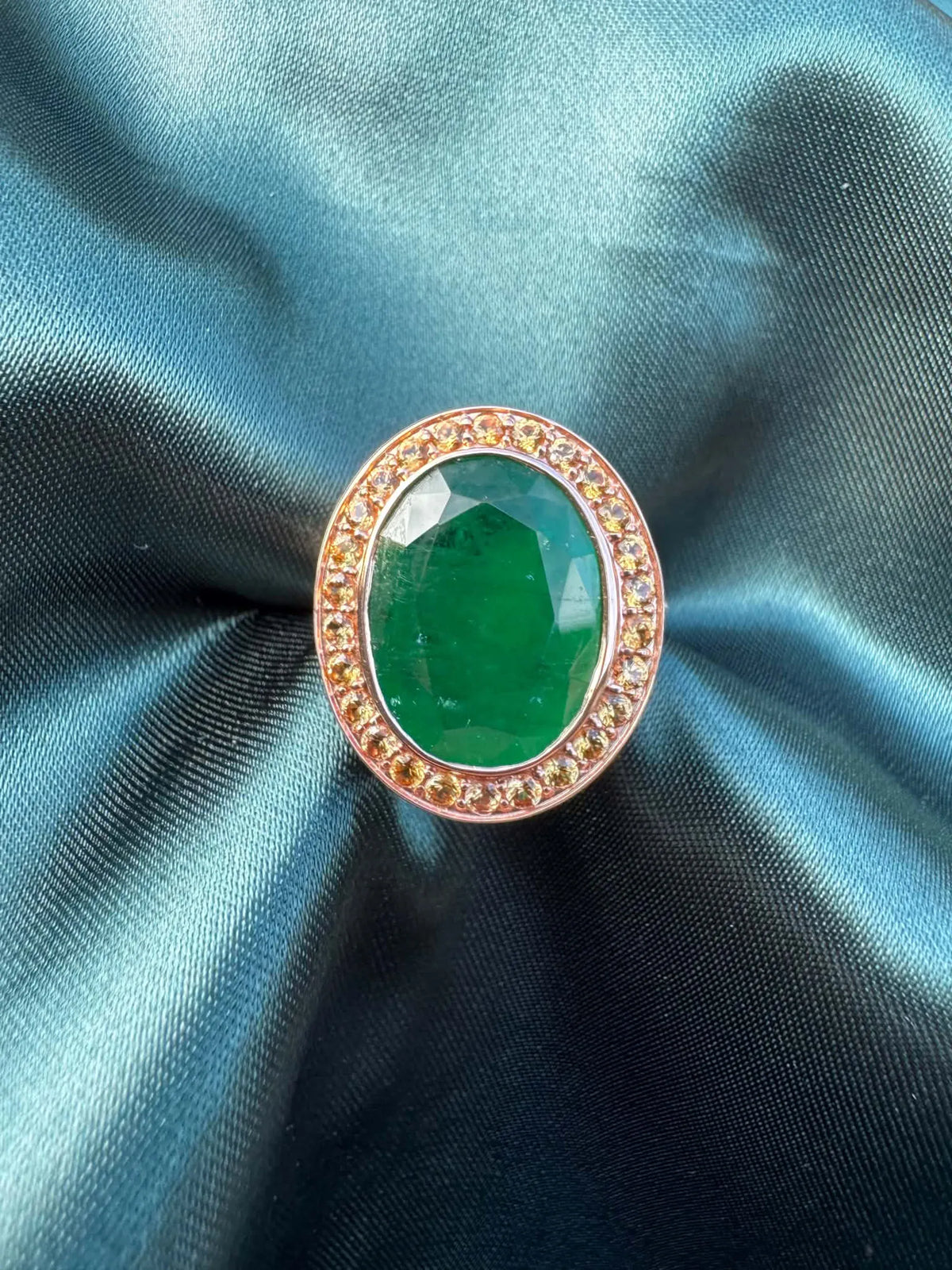 Emerald and orange sapphire cocktail ring in 14ct rose gold, front view showing oval emerald in sapphire halo