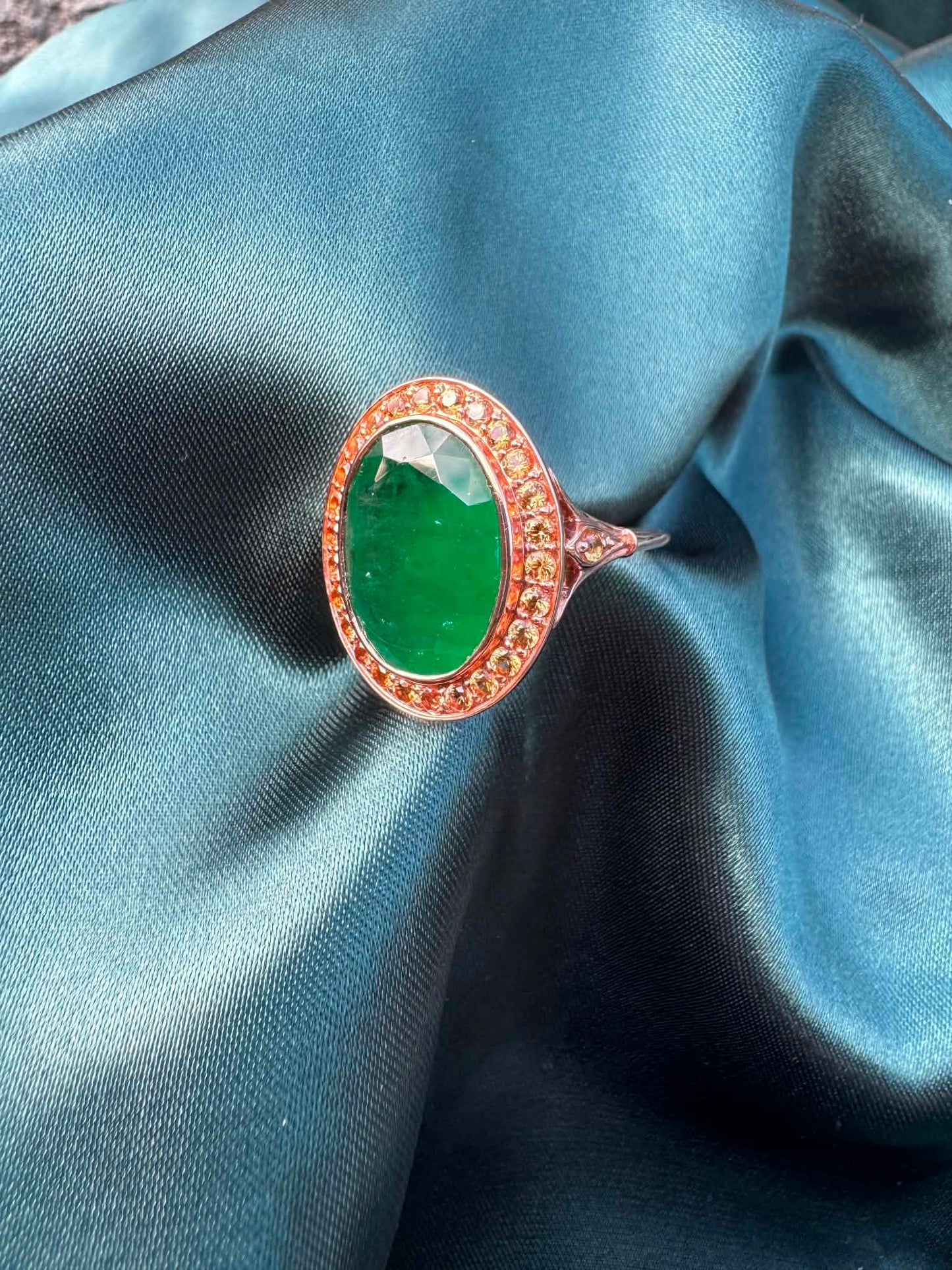 Emerald and orange sapphire cocktail ring in 14ct rose gold, angled top view showing oval emerald and sapphire halo