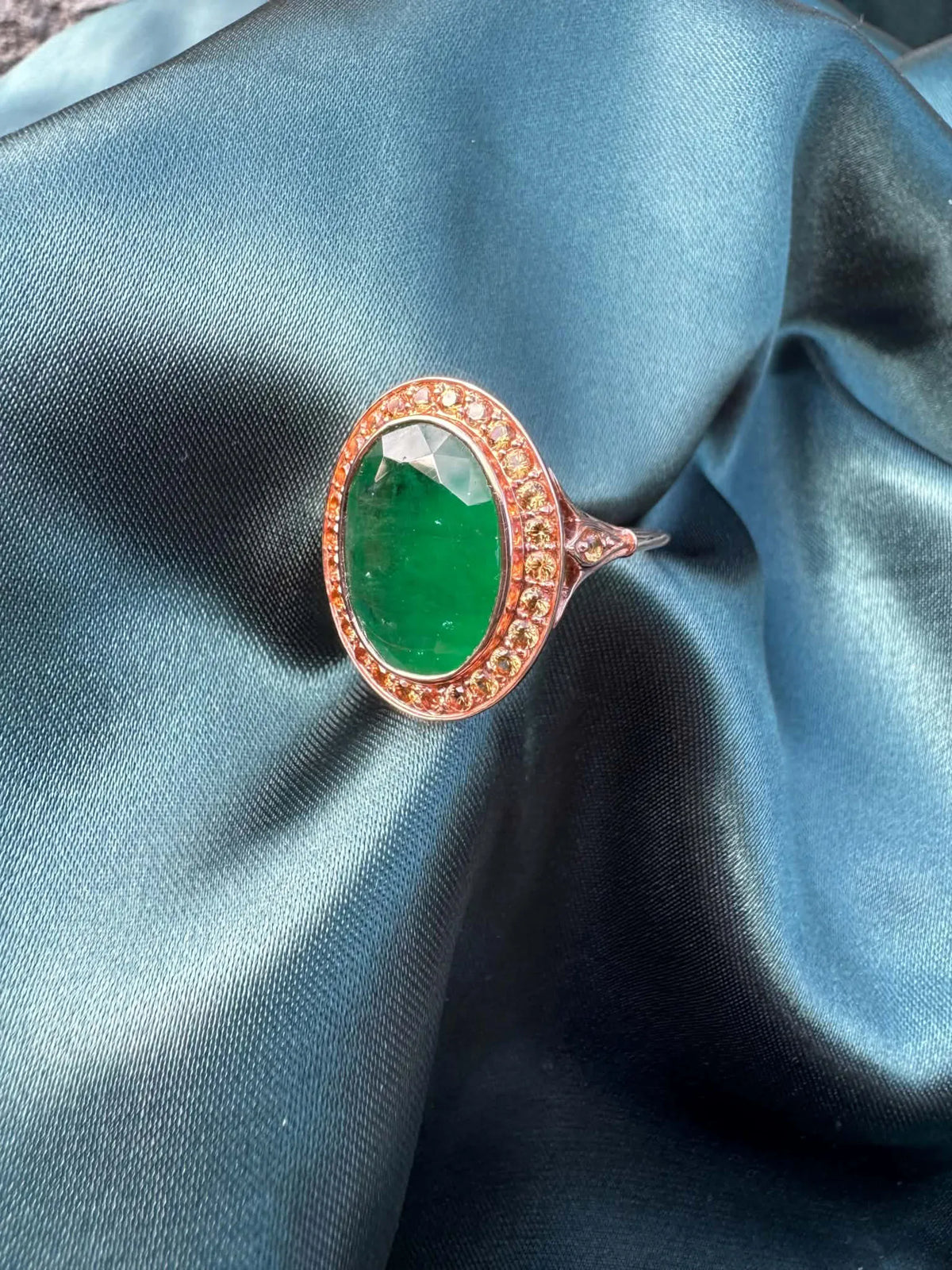 Emerald and orange sapphire cocktail ring in 14ct rose gold, angled top view showing oval emerald and sapphire halo