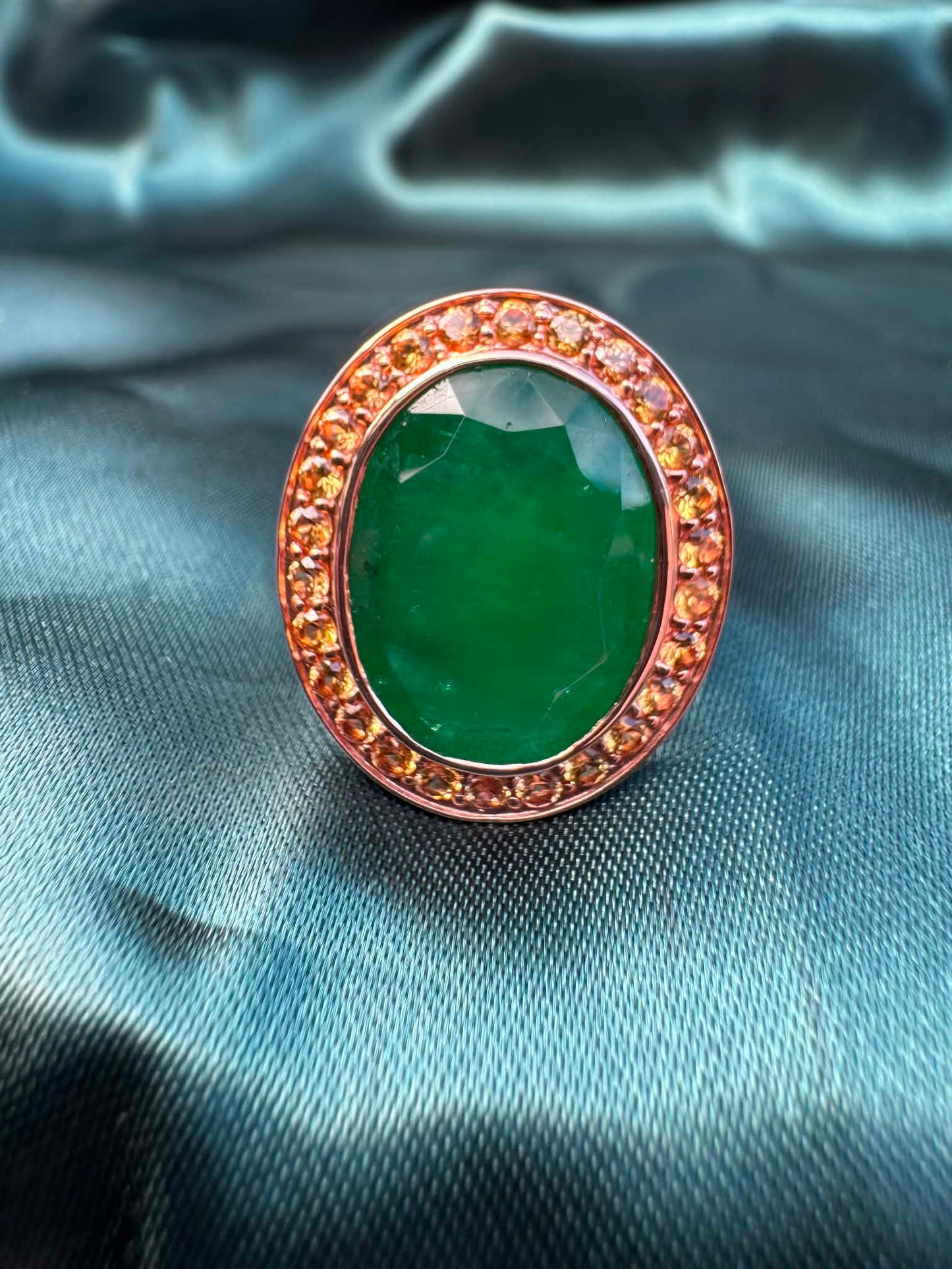 Emerald and orange sapphire cocktail ring in 14ct rose gold, angled front view showing oval emerald in sapphire halo