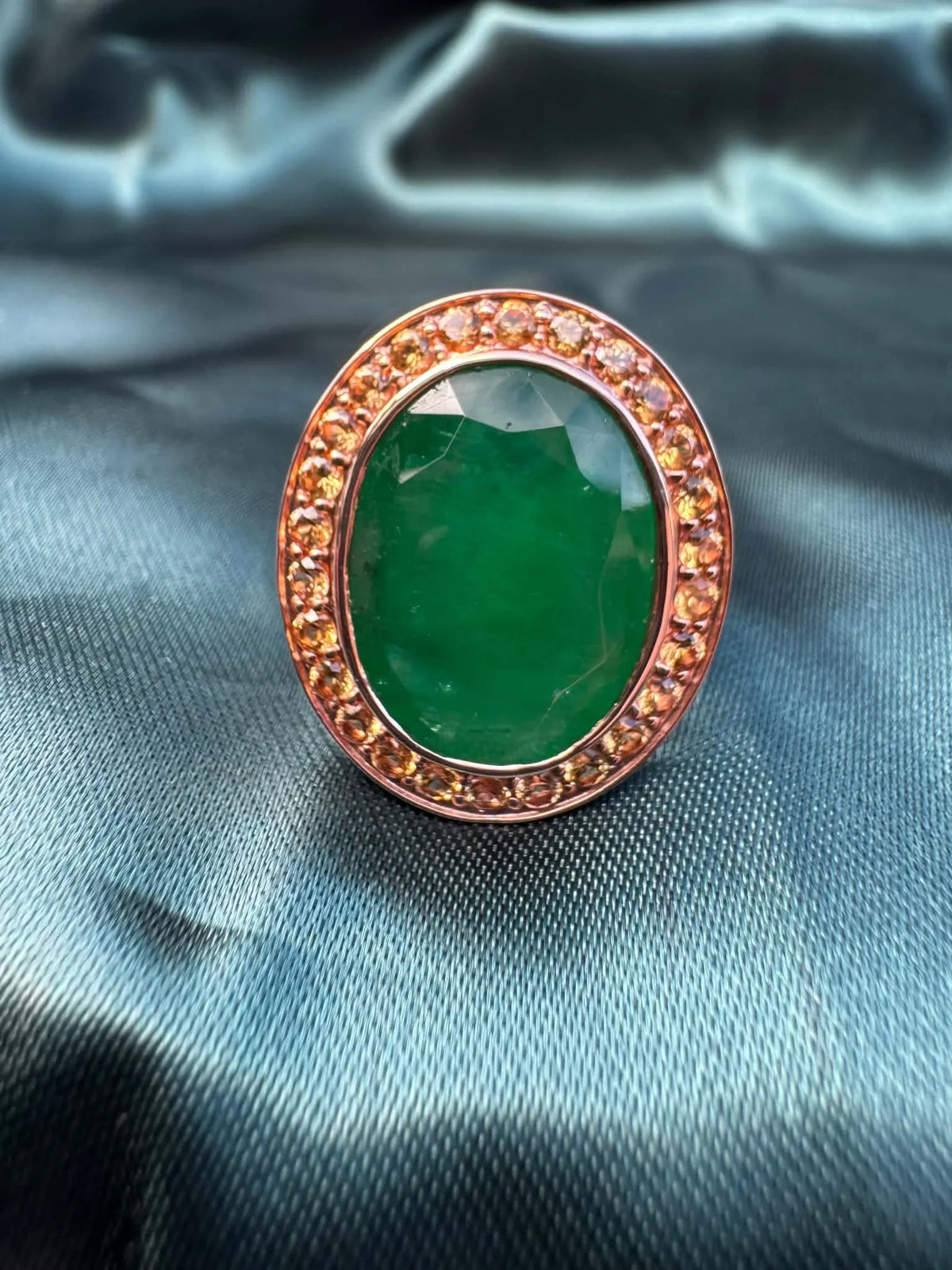 Emerald and orange sapphire cocktail ring in 14ct rose gold, angled front view showing oval emerald in sapphire halo