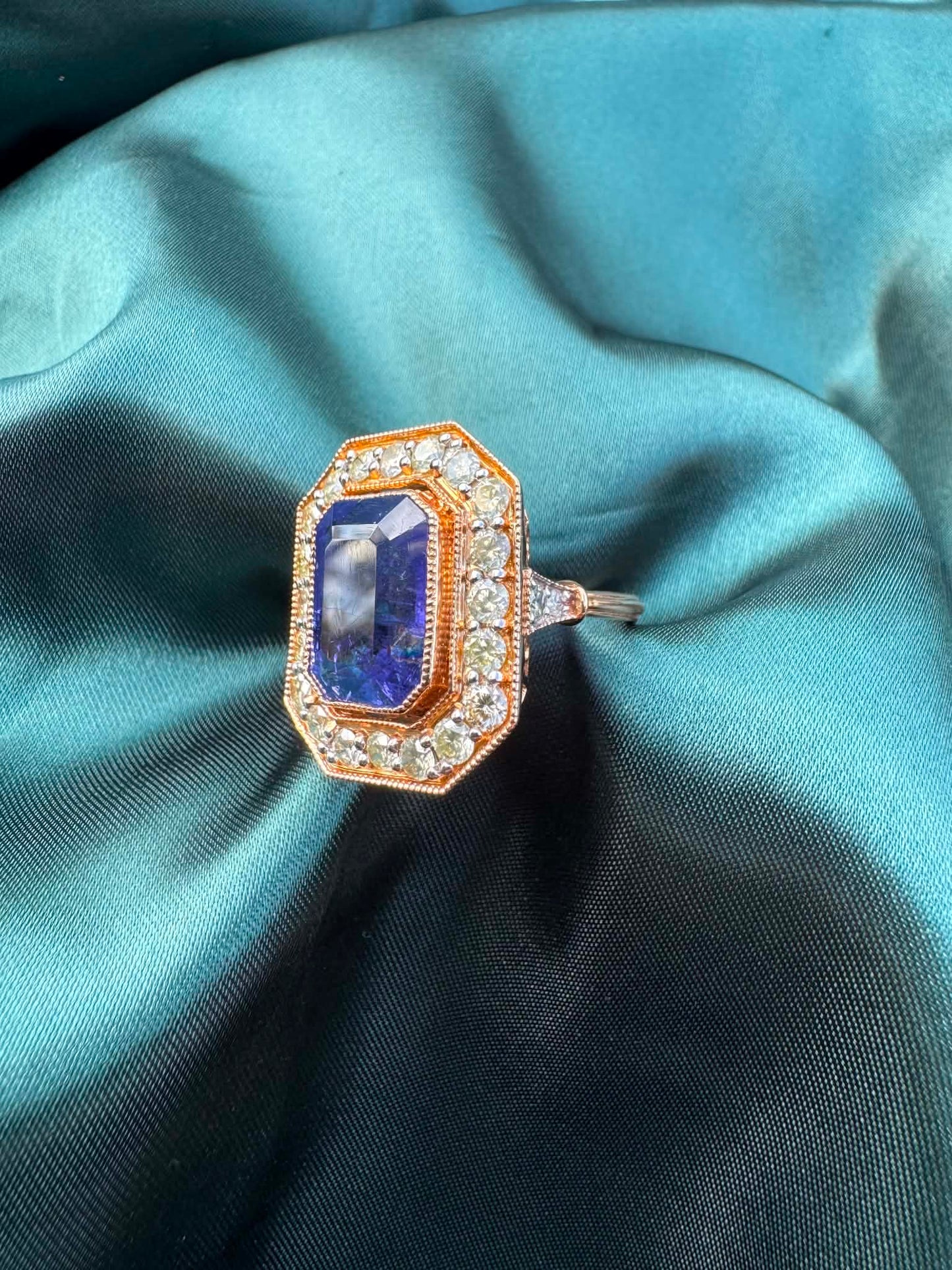Tanzanite and diamond halo ring in 18ct rose gold, angled top view showing emerald-cut tanzanite in octagonal diamond halo