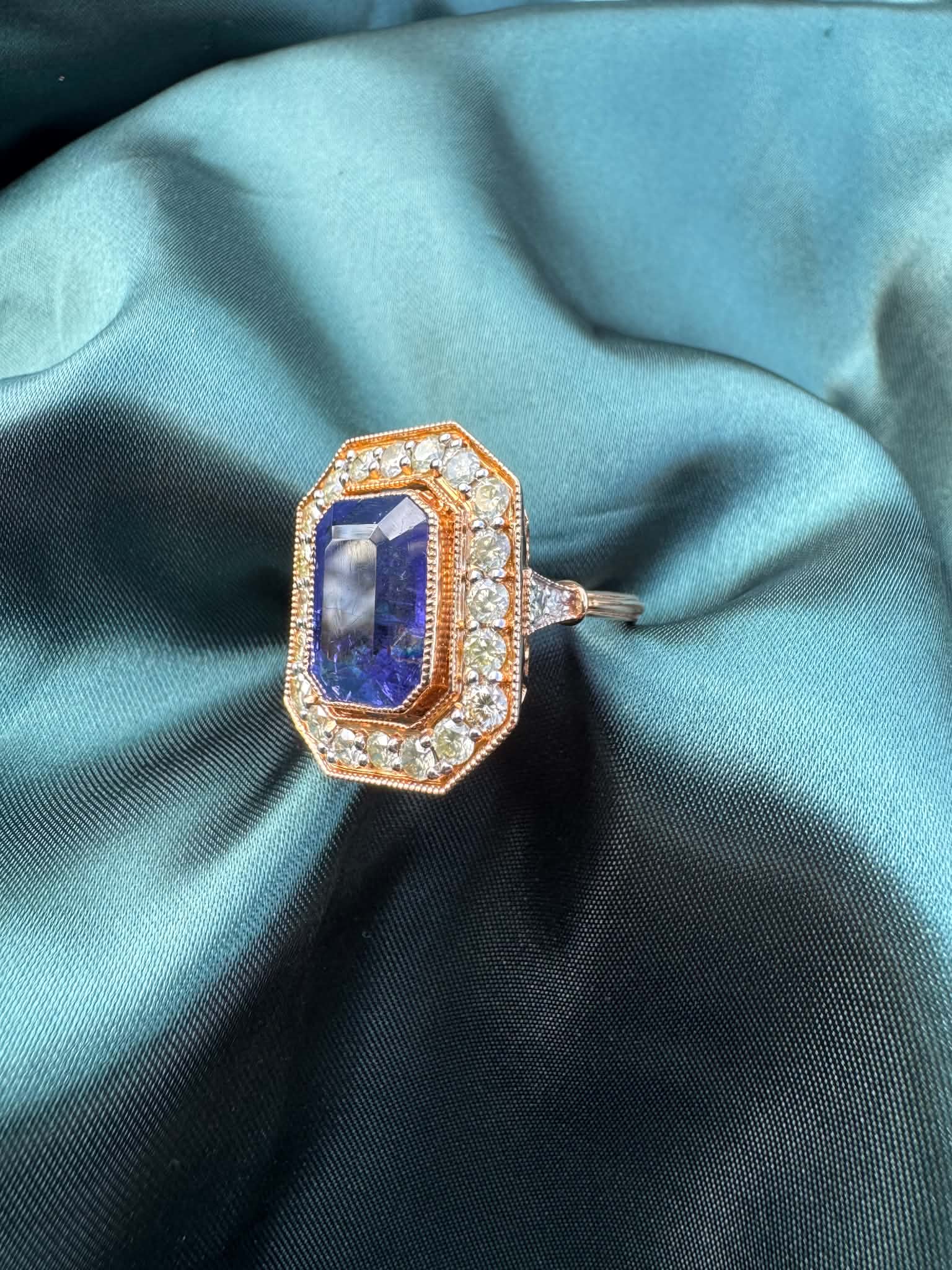 Tanzanite and diamond halo ring in 18ct rose gold, angled top view showing emerald-cut tanzanite in octagonal diamond halo