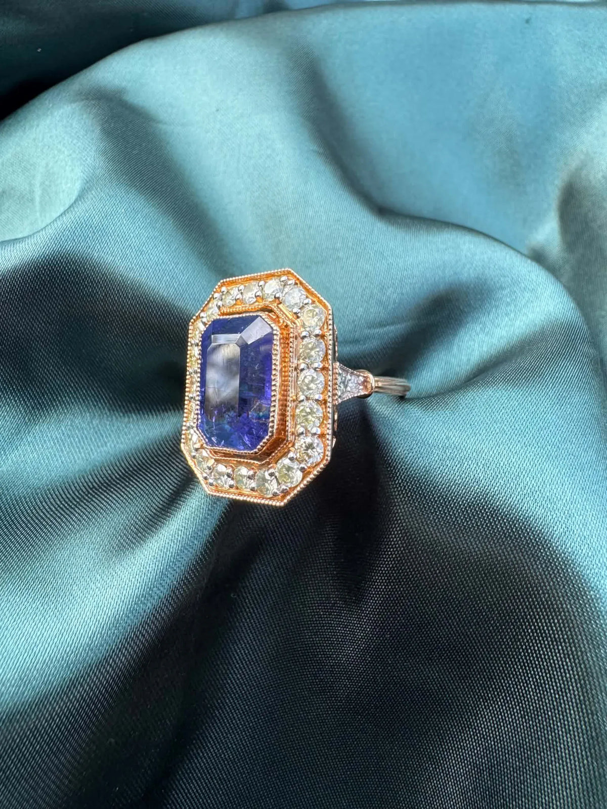 Tanzanite and diamond halo ring in 18ct rose gold, angled top view showing emerald-cut tanzanite in octagonal diamond halo