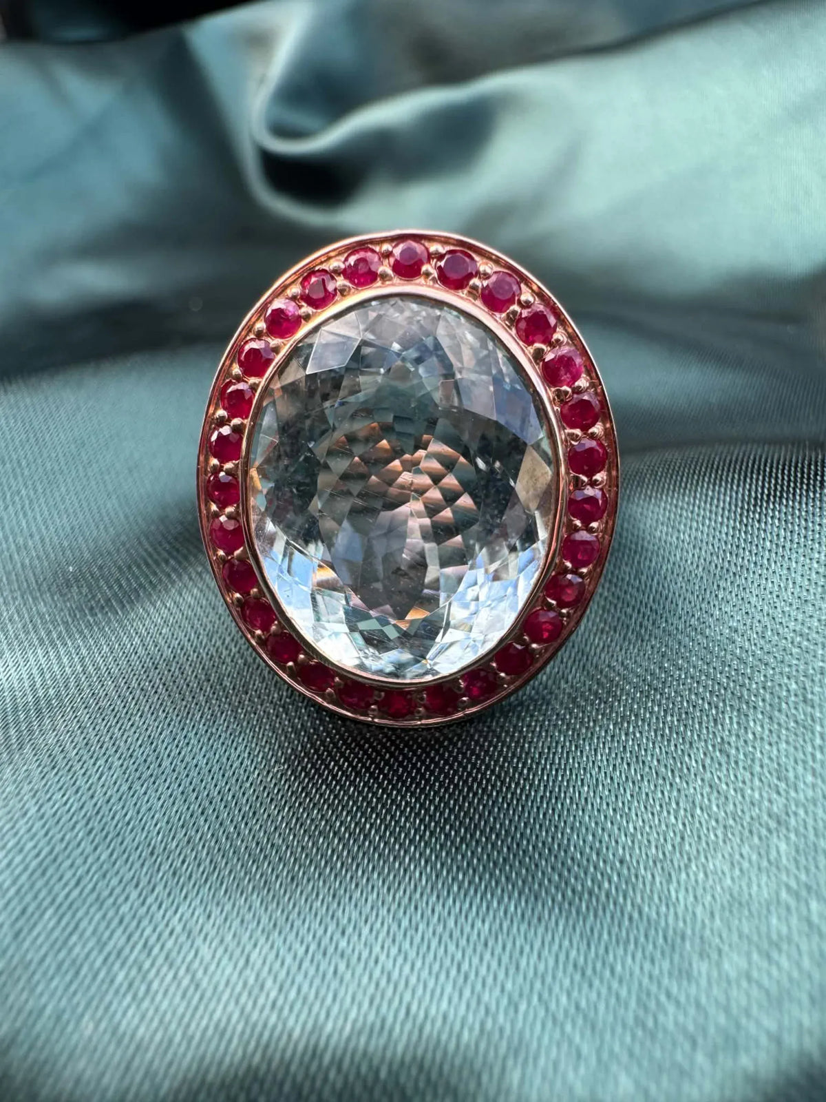 Aquamarine and gemstone halo ring in 14ct rose gold, close-up showing oval aquamarine and red gemstone halo