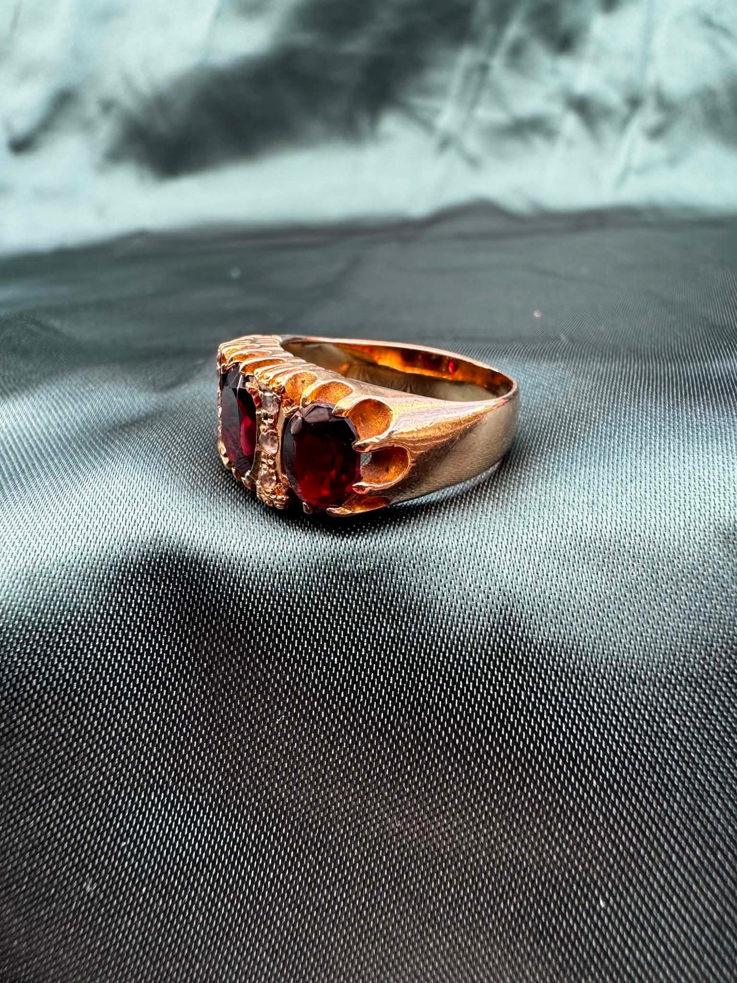 Garnet and paste three stone ring in 9ct gold on teal fabric, angled top view showing garnet and paste stones
