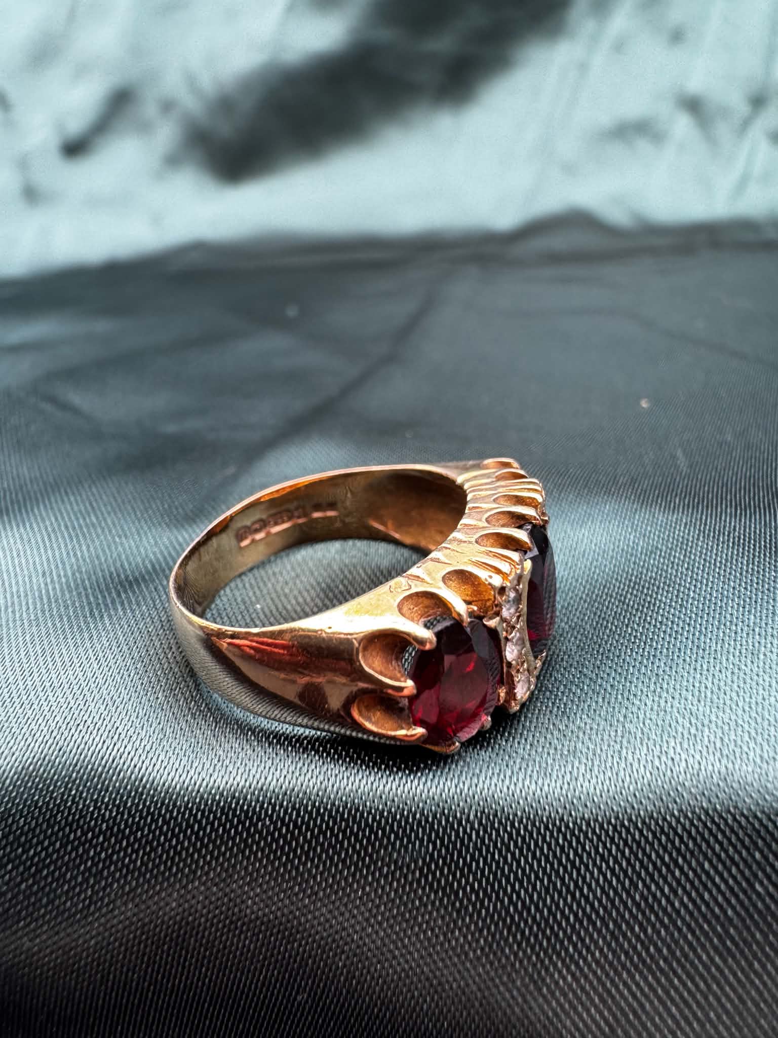 Garnet and paste three stone ring in 9ct gold on teal fabric, angled view showing garnet and paste stones